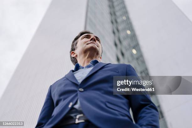 confident mature businessman standing in front of an office tower in the city - low angle view stockfoto's en -beelden