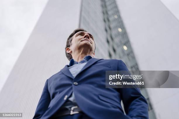 confident mature businessman standing in front of an office tower in the city - low angle view imagens e fotografias de stock