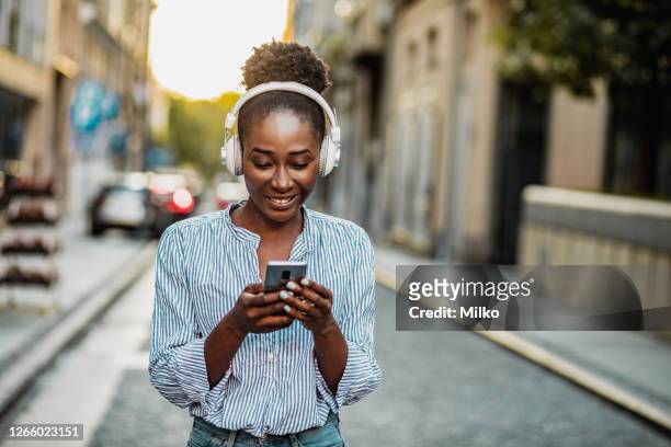 mulher com fones de ouvido usando telefone na rua - escutando - fotografias e filmes do acervo