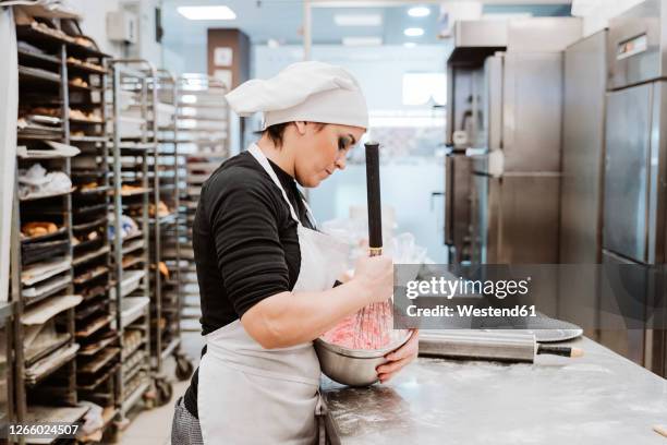 female baker mixing cake batter in bowl at commercial kitchen - female whipping stock-fotos und bilder