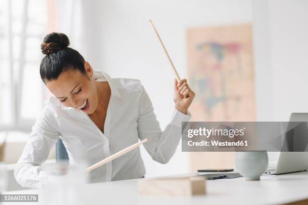 cheerful female entrepreneur playing drumsticks on desk while screaming in home office - baqueta instrumento musical - fotografias e filmes do acervo