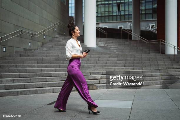 fashionable young businesswoman walking while holding diary in city - walking side by side stockfoto's en -beelden