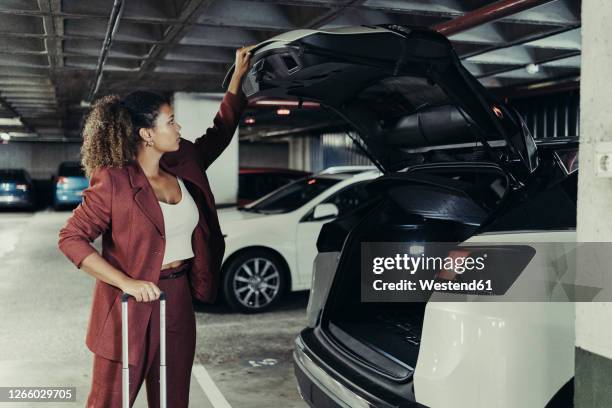 young female professional on business trip closing car trunk at parking garage - closing car boot fotografías e imágenes de stock