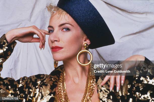 Studio portrait of British singer-songwriter Annie Lennox, of The Eurythmics, wearing a gold and black outfit, with a blue hat, and gold hoop...