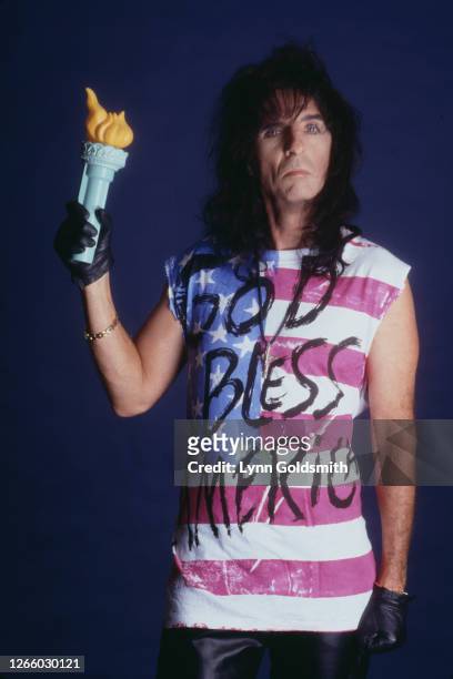Studio portrait of American rock singer Alice Cooper wearing a t-shirt with an American Flag design and the legend 'God Bless America' across the...