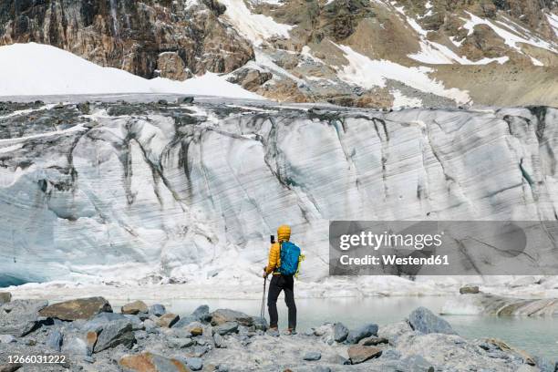 man hiking while looking at melting glacier - european alps stock pictures, royalty-free photos & images