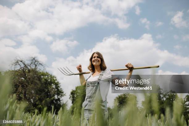 young woman with hay fork standing in a grain field in the countryside - farmer portrait stock-fotos und bilder
