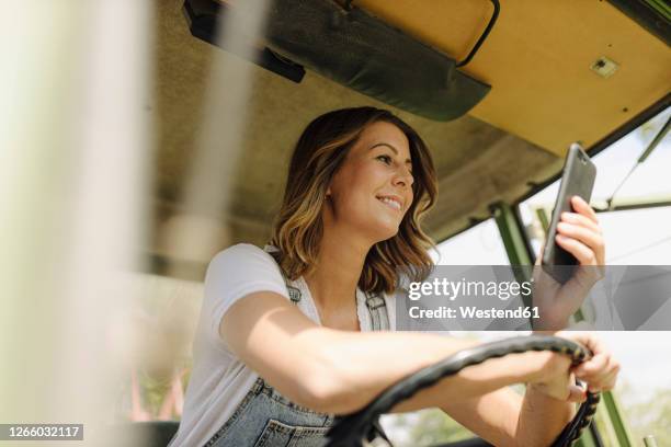 smiling young woman using mobile phone in a tractor - bauer traktor stock-fotos und bilder