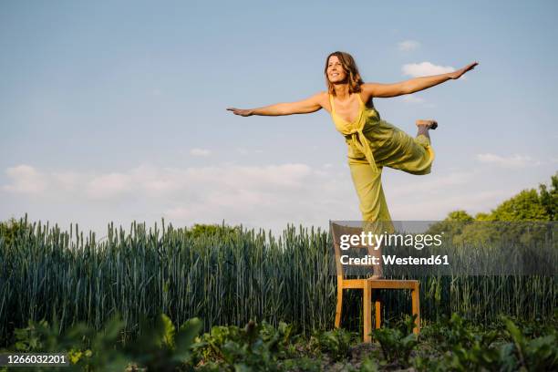 young woman standing on a chair in the countryside pretending to fly - gleichgewicht stock-fotos und bilder