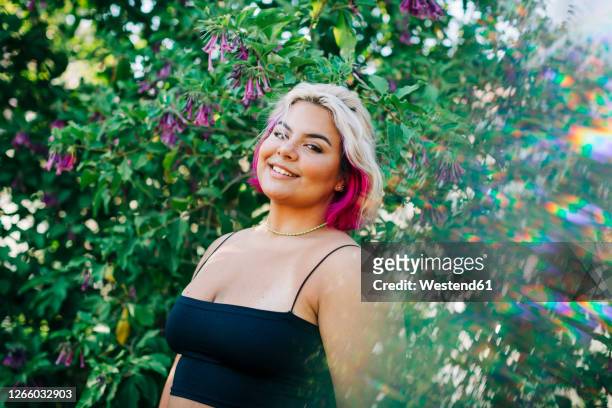 smiling large build woman standing near flowering plant outdoors - buxom blonde stock pictures, royalty-free photos & images