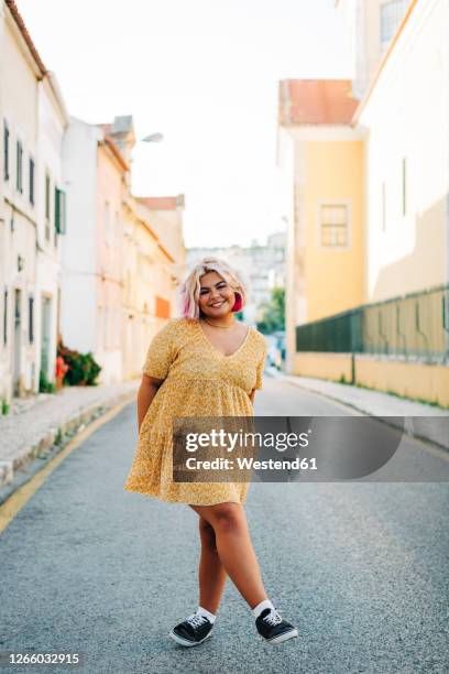 smiling plus size woman standing with crossed leg on road - plump girls stock pictures, royalty-free photos & images