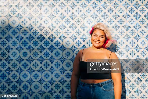 smiling young woman standing against patterned wall - buxom blonde stock pictures, royalty-free photos & images