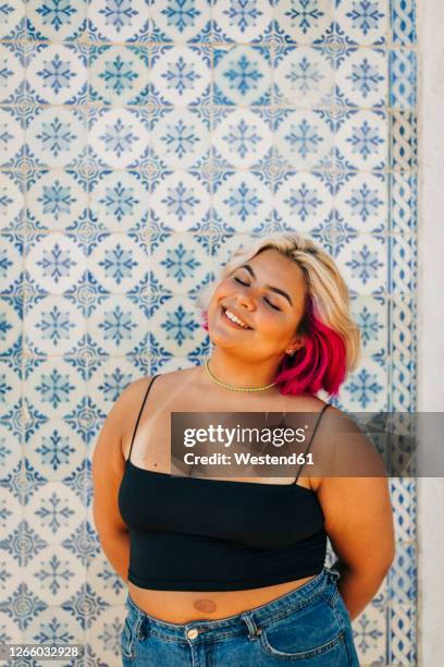 young woman standing with hand behind back against wall - chubby girl style photos et images de collection