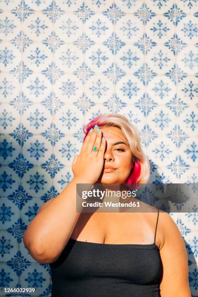 woman hiding half face with one hand against patterned wall - blond hair young woman sunshine stockfoto's en -beelden