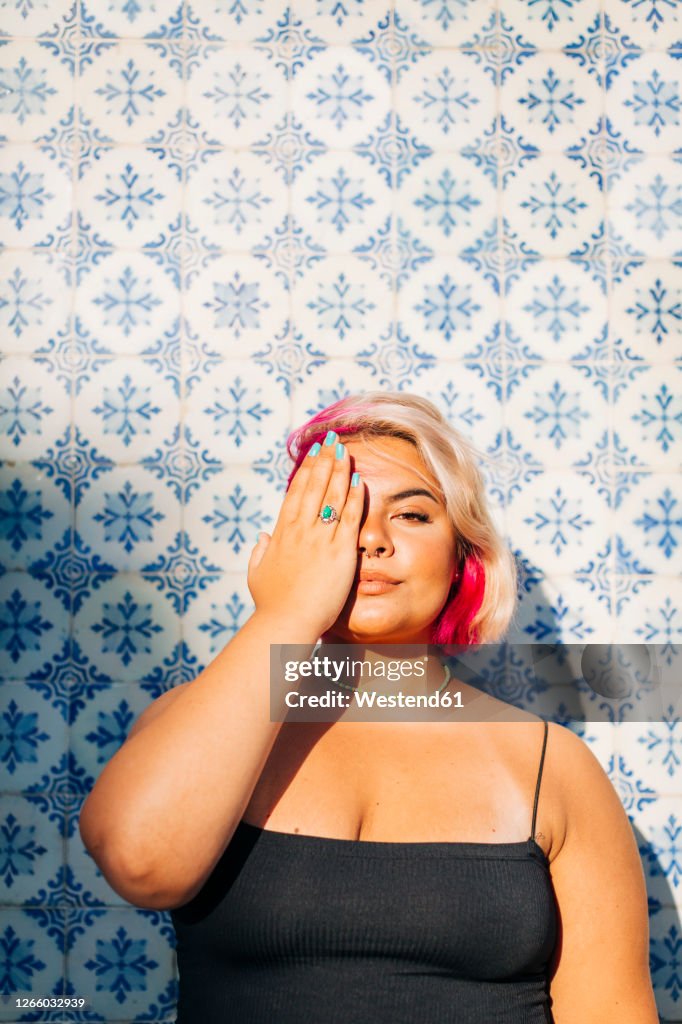 Woman hiding half face with one hand against patterned wall