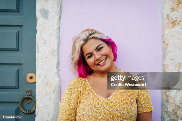 smiling young woman standing against wall - reflexo cabelo pintado imagens e fotografias de stock