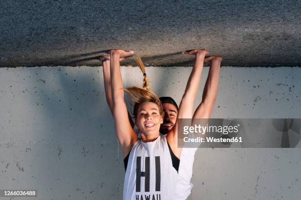 smiling couple practicing handstands on road against wall in city - fare la verticale sulle mani foto e immagini stock