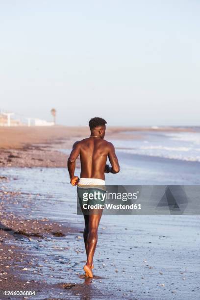 shirtless young man running at shore against clear sky - hunky guy on beach stock pictures, royalty-free photos & images