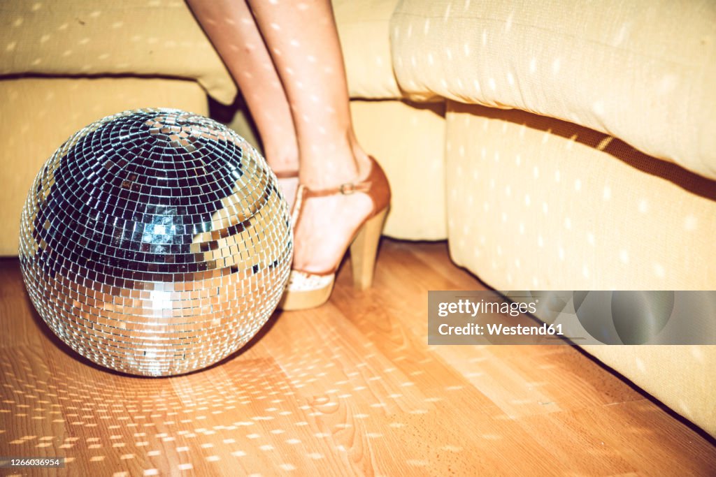 Young woman wearing high heels standing by disco ball on floor in party