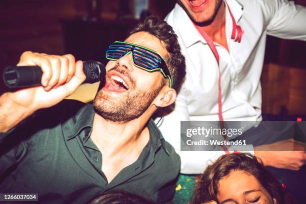 close-up of young man singing karaoke while enjoying with friends in party - karaokê - fotografias e filmes do acervo