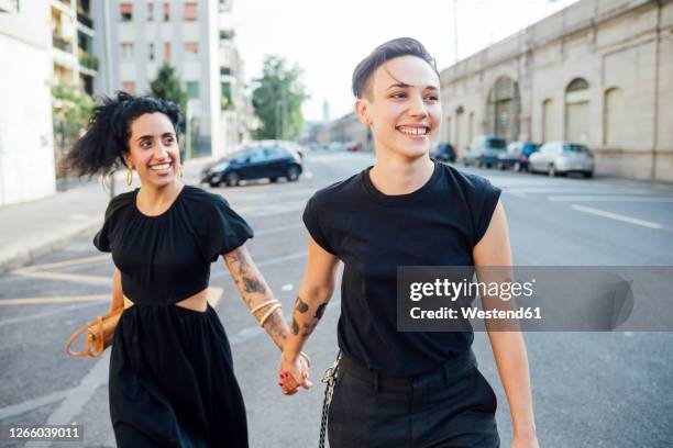 smiling lesbian couple walking in city - lesbians stock-fotos und bilder