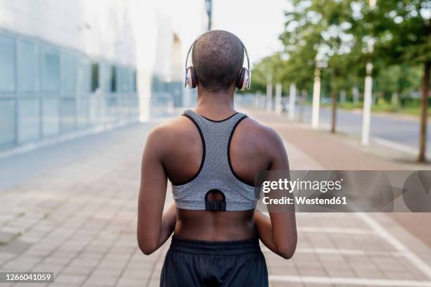 young woman with shaved head listening music through headphones while standing on footpath - shaved head fotografías e imágenes de stock