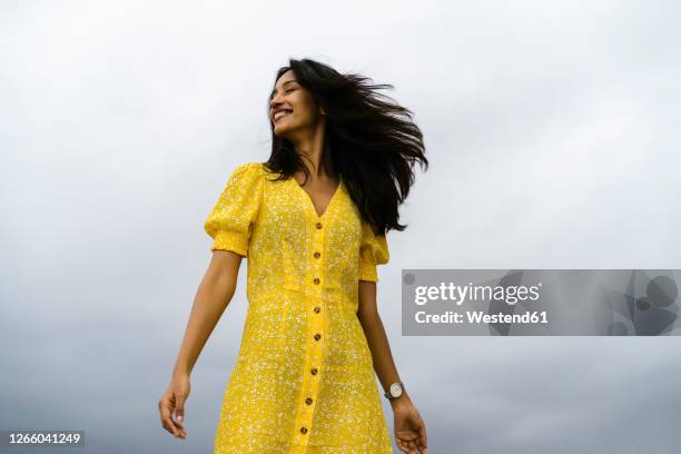 happy young woman standing against cloudy sky - sommerkleid stock-fotos und bilder