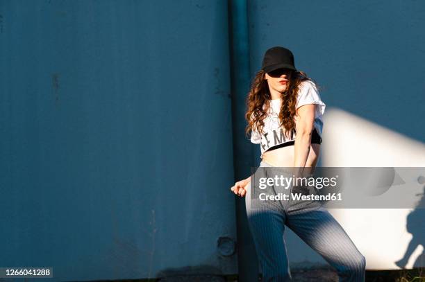 female hip-hop dancer puckering lips while dancing against white wall during sunny day - bauchfreies oberteil stock-fotos und bilder