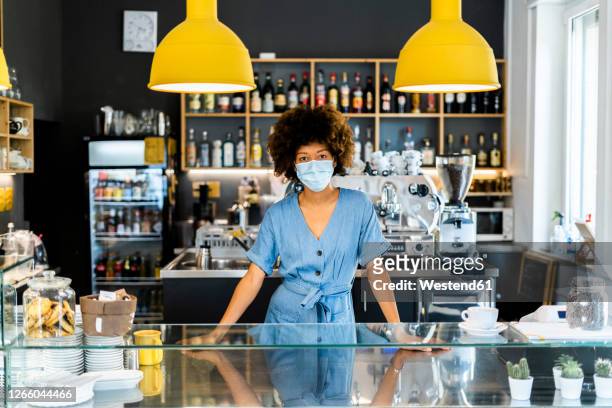 young female owner wearing mask standing at counter in coffee shop - small business mask stock pictures, royalty-free photos & images