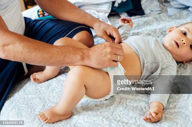 father with baby boy lying on bed, changing diapers - baby nappy stock-fotos und bilder