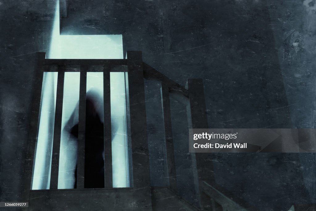 Looking up at a spooky, blurred ghostly figure standing on top of a stairs. With an old, grunge textured edit.