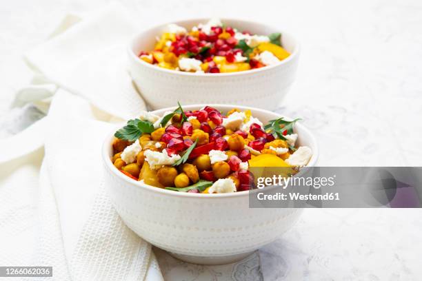 two bowls of vegetarian salad with chick-peas, turmeric, bell peppers, tomatoes, parsley, feta cheese and pomegranate seeds - tropical fruit stock pictures, royalty-free photos & images