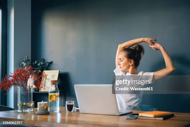 tired businesswoman stretching arms while sitting at desk in home office - stretching at work stock pictures, royalty-free photos & images