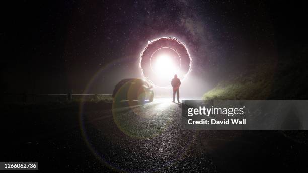 a lone car, parked on the side of the road, underneath a glowing ufo portal, with a hooded figure, on a spooky, scary, rural, country road. on a foggy winters night - flying saucer stock pictures, royalty-free photos & images