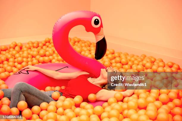 cheerful young woman with inflatable flamingo lying in orange ball pit - adult ball pit stock-fotos und bilder