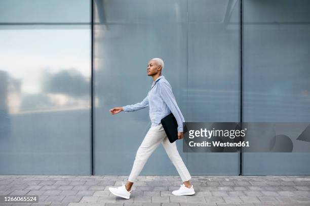 businesswoman with folder walking against building in city - vista laterale foto e immagini stock