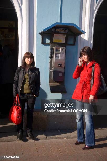 Une jeune femme avec un sac à mains rouge se tient debout à côté d'un téléphone public pendant qu'une autre jeune femme téléphone avec son mobile ,...