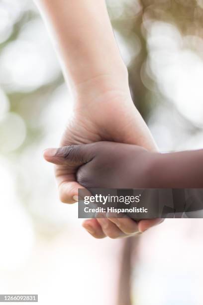 unkenntliche kaukasische mutter hält die hand ihres schwarzen sohnes - black and white holding hands stock-fotos und bilder