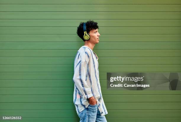 a young afro-haired man listens to music on a green background - adolescent africain stock pictures, royalty-free photos & images