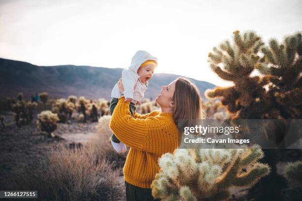 a woman with a baby is standing near a cactus in the desert - bush baby fotografías e imágenes de stock