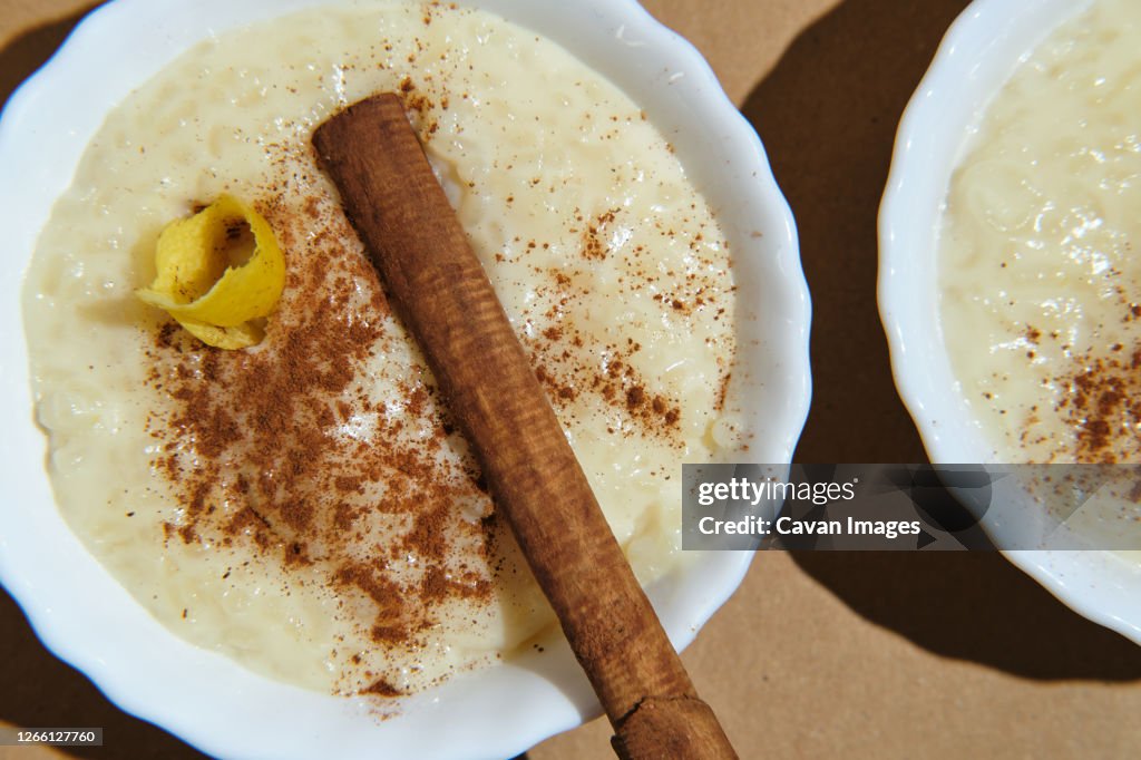 Foreground rice pudding decorated with lemon peel and cinnamon sticks