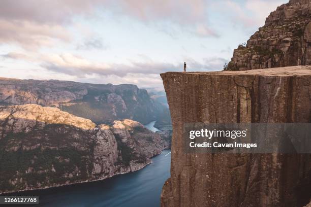 man standing at edge of cliff at preikestolen, norway - cliff edge stock-fotos und bilder