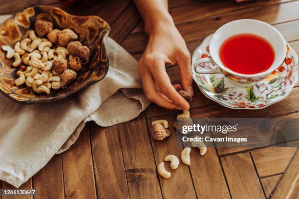 cup of hibiscus tea, hand and dry fruits on top of a table - eating nuts stock-fotos und bilder