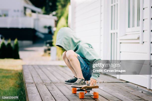 boy sat on a skateboard with his hood up hiding his face - skater boy hair stock pictures, royalty-free photos & images