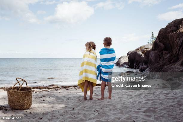 boy and girl stood on the beach wrapped in towels looking at the ocean - towel lined stock pictures, royalty-free photos & images