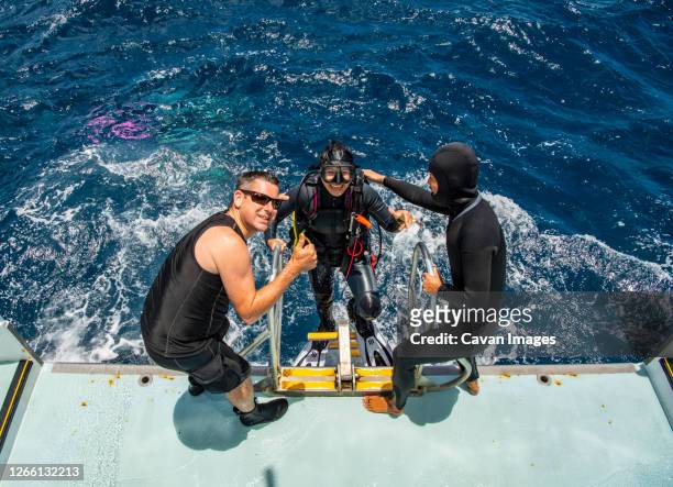 two friends helping diver back on board of dive boat - woman diving board stock pictures, royalty-free photos & images