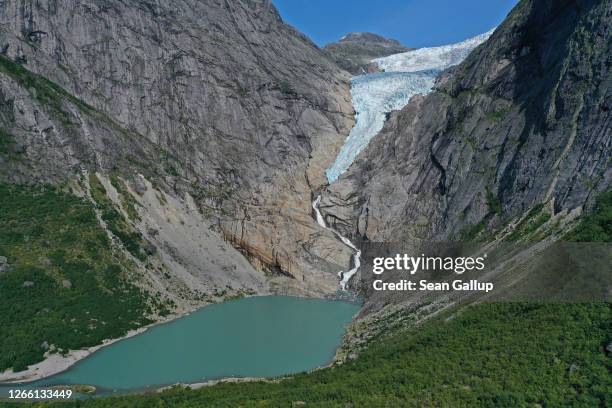 In this aerial view from a drone the melting Briksdal glacier lies above rocks it ground smooth and once covered in ice next to a lake created by...