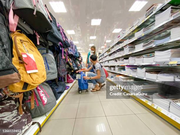 little girl with her mother choosing between big variety of backpacks for new school year during the covid-19 pandemic - stock photo - school supplies mask stock pictures, royalty-free photos & images