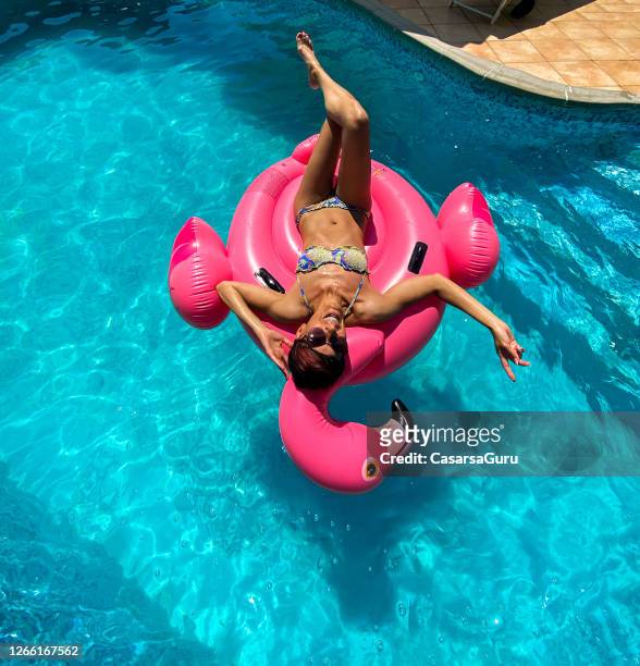 sorglos erwachsene frau entspannen auf aufblasbaren floß im schwimmbad - flamingos stock-fotos und bilder