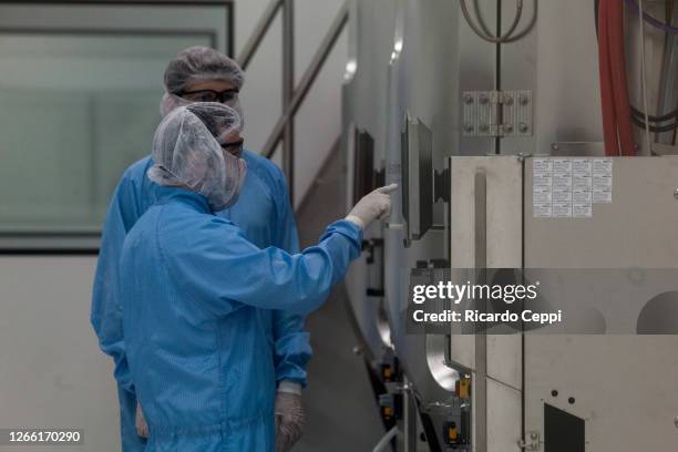 Laboratory workers wearing PPE check a screen of a centrifuge machine at the production plant of mAbxience biotechnology company on August 13, 2020...